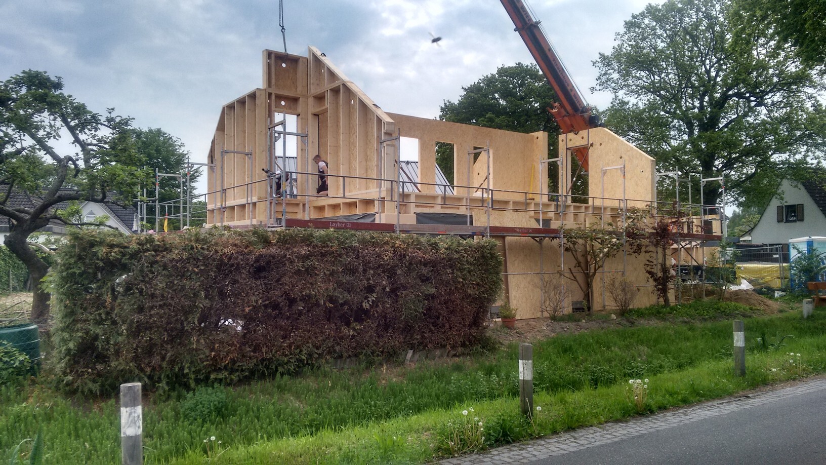Holzbau eines Einfamilienhauses im Aufbau, Bauarbeiter auf Gerüst, Kran im Hintergrund