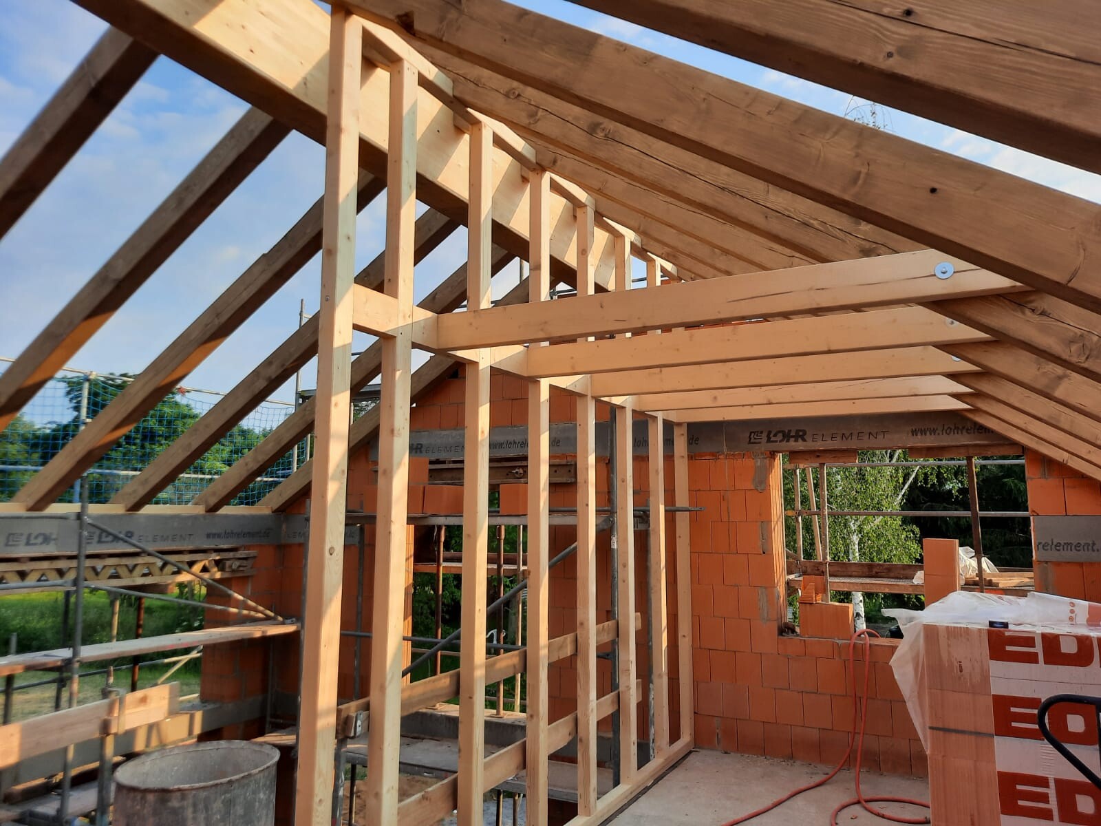 Bau einer Holzkonstruktion: Dachstuhlrahmen und Innenwand aus Ziegelsteinen auf einer Baustelle.