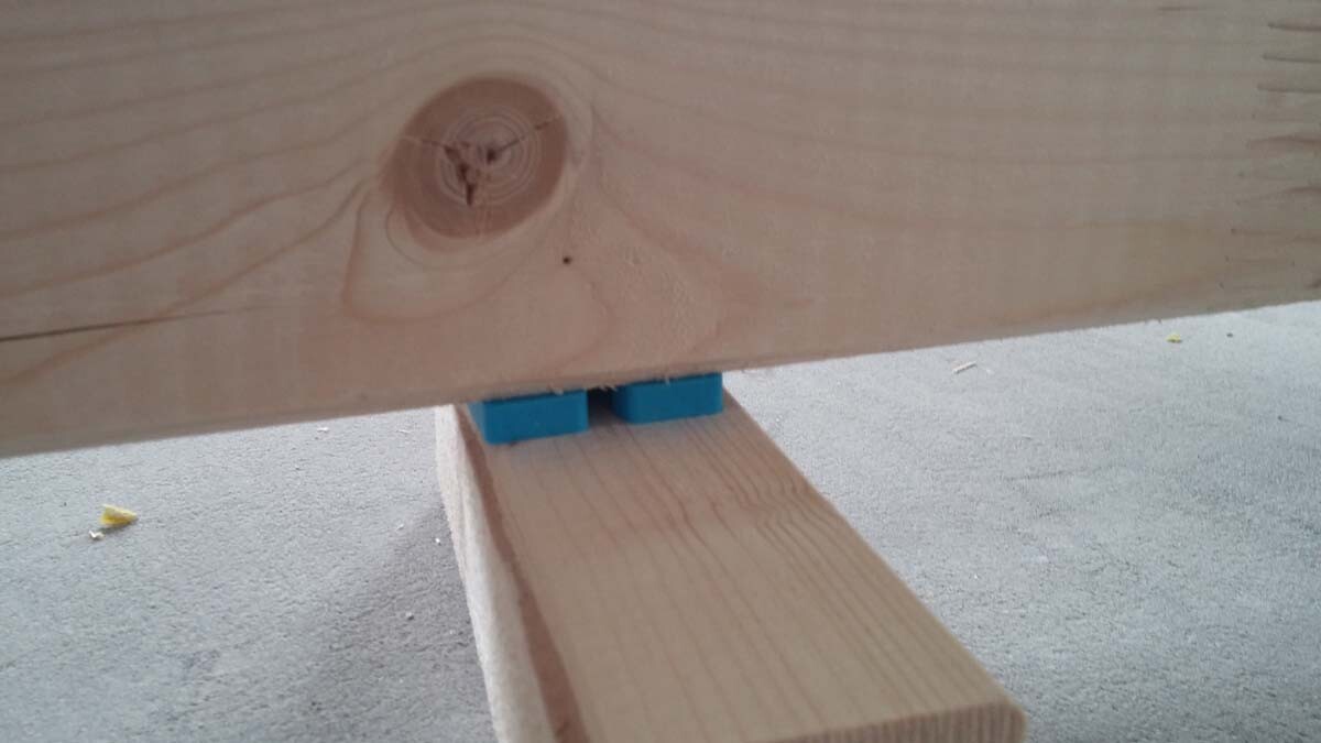 Nahaufnahme eines Holzbalkens mit blauen Spannblöcken zwischen Bauteilen