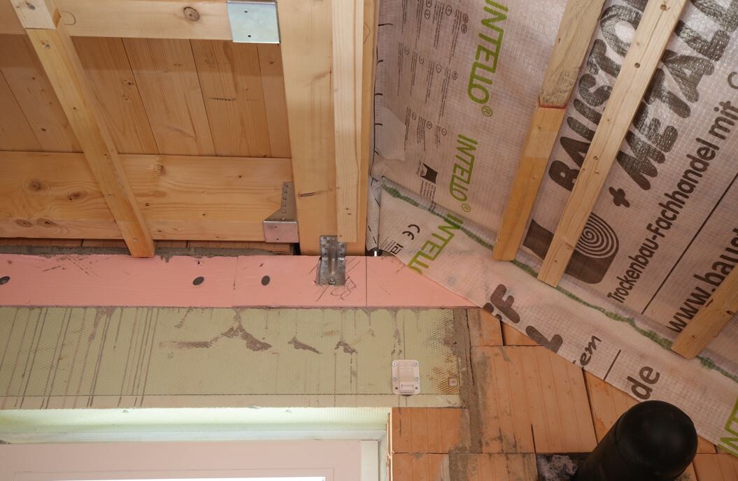 Dachboden mit Holzrahmen, pinke Dämmplatten, Metallbeschläge und Rohre.