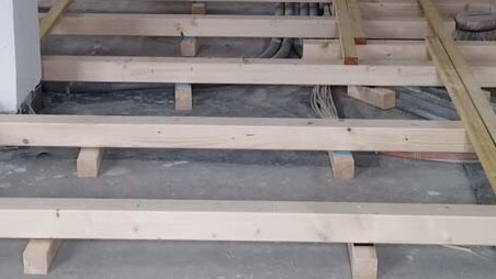Holzrahmenkonstruktion im Rohbau mit sichtbaren Bodenbalken und Unterbau.