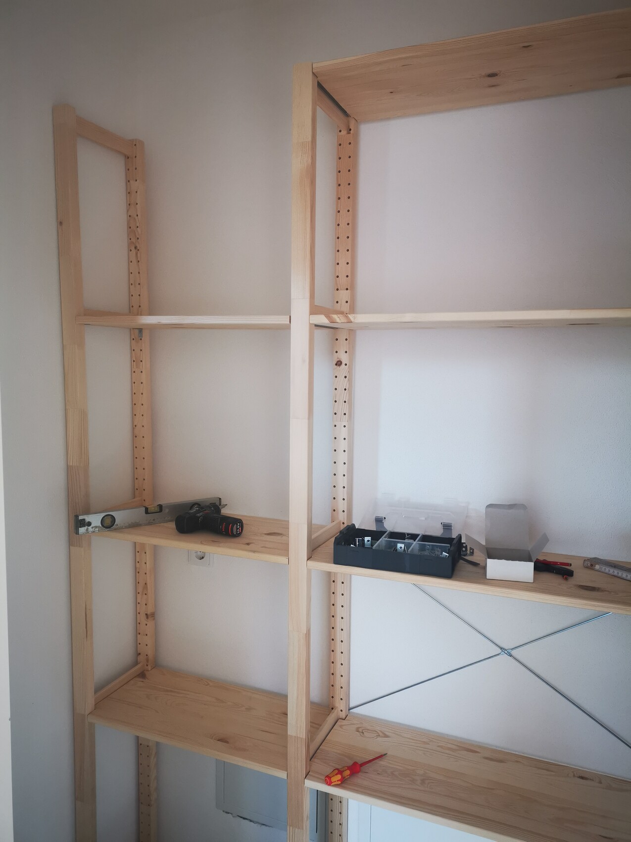 Offenes Holzregal mit verstellbaren Pfosten; Werkzeugbox, Bohrmaschine und Level auf Brettern.