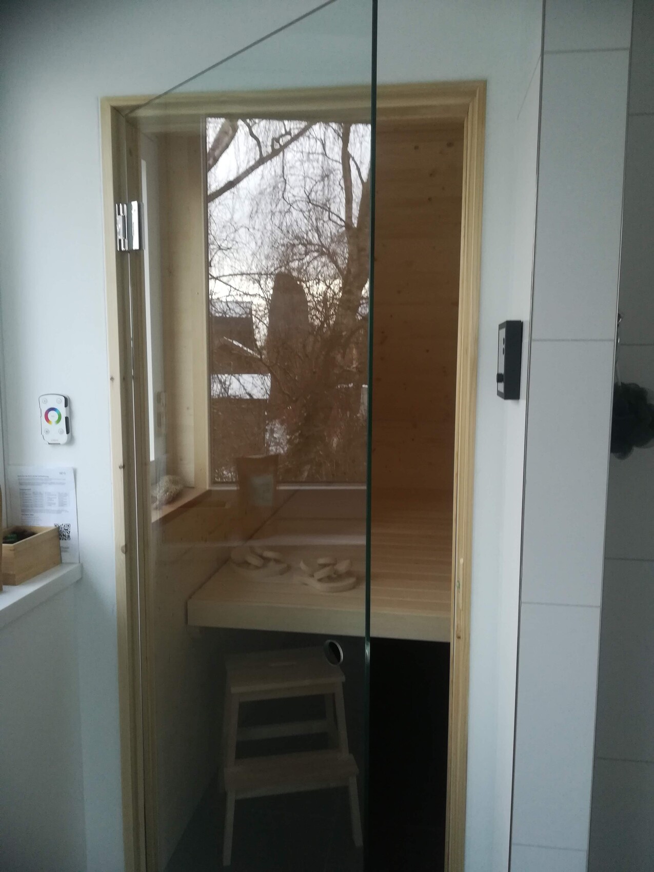 Sauna mit Holzbank hinter Glaswand; winterliche Baumlandschaft draußen sichtbar.