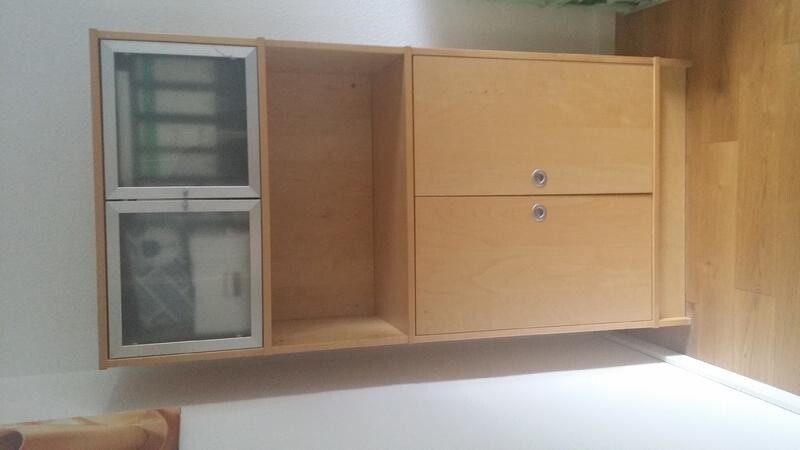 Heller Holzkabinettsschrank mit Glasfronten steht im Wohnzimmer auf Holzboden.
