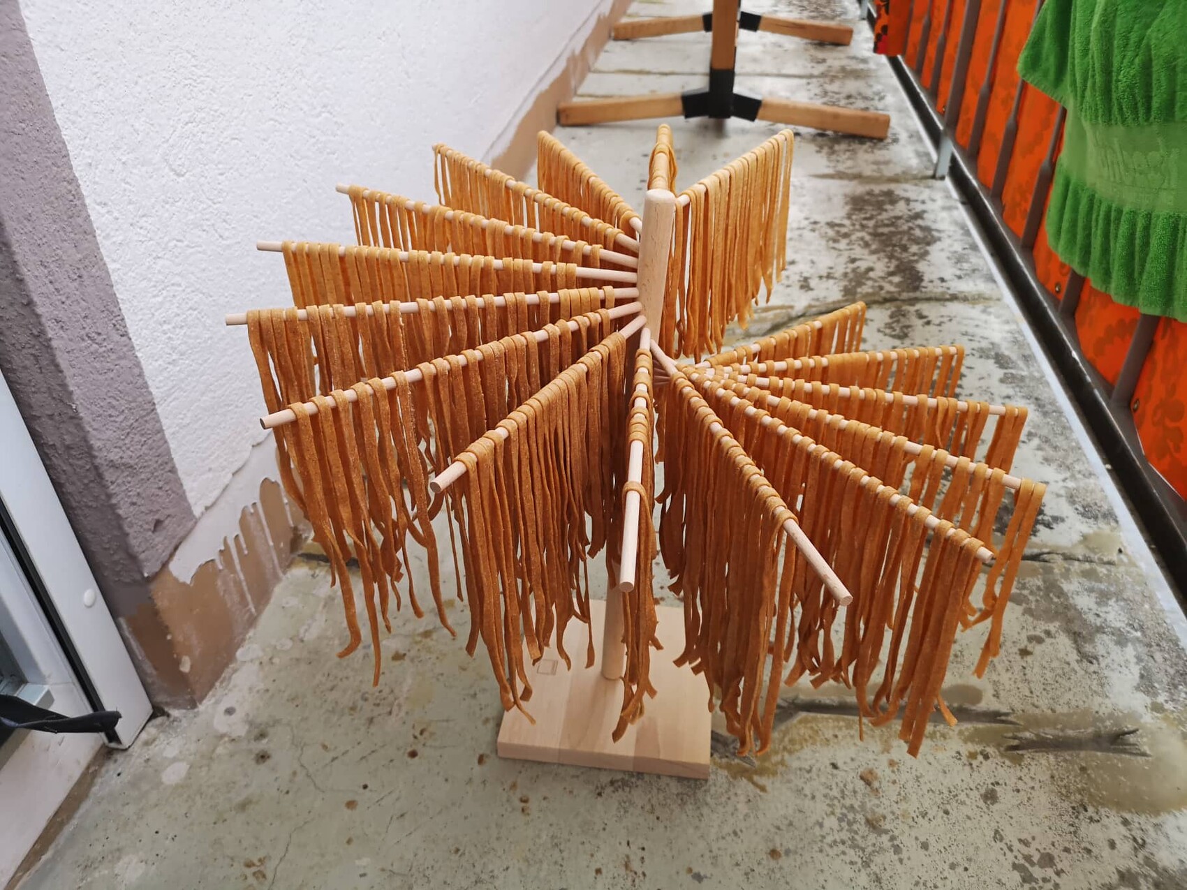 Holzskulptur auf Balkon mit radial angeordneten Armen und braunen Fransen