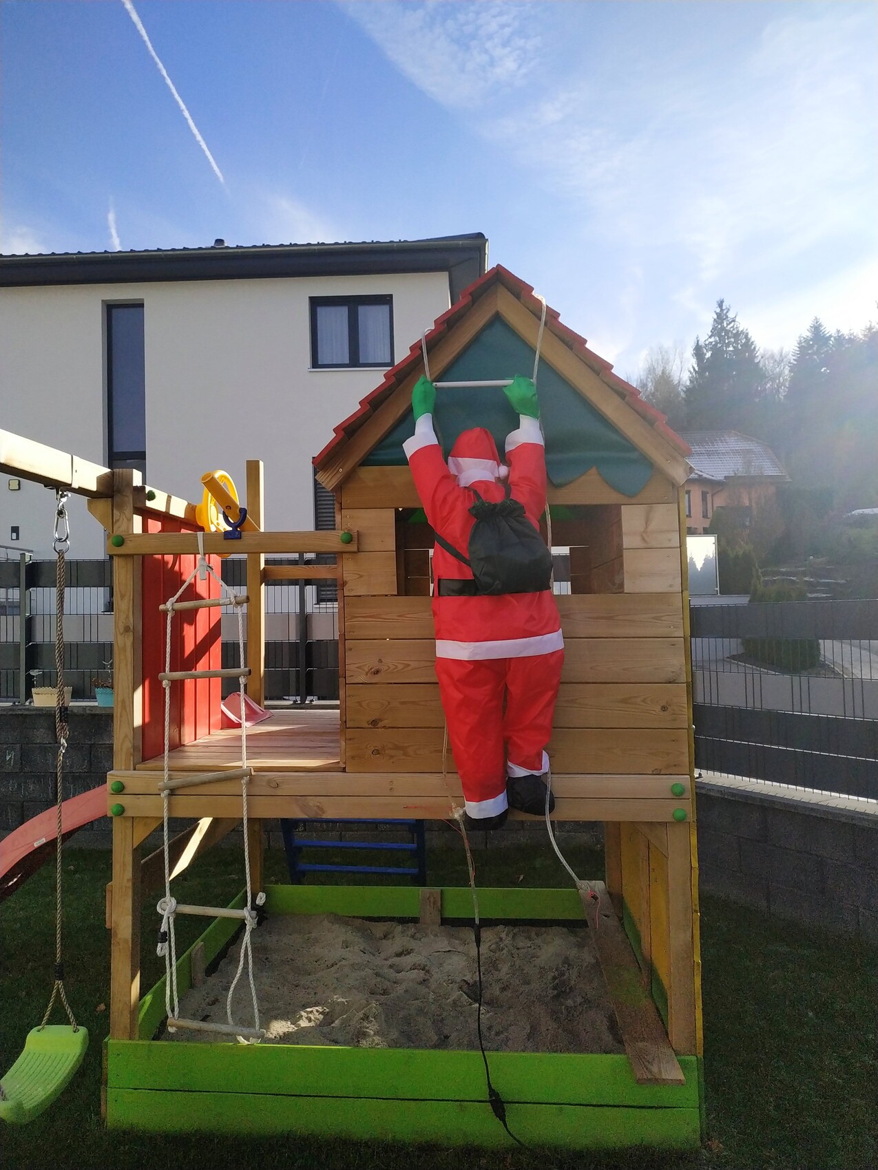 Person in Santa-Kostüm klettert mit Seil am Spielhaus aus Holz über Sandkasten.