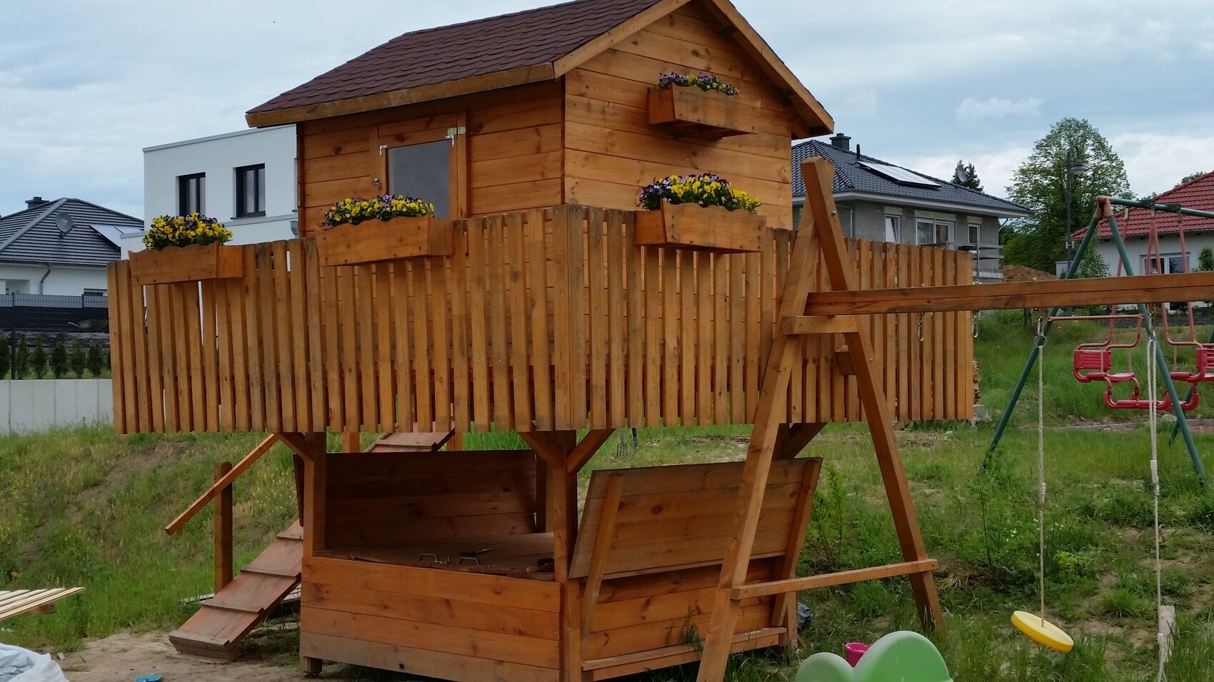 Holz-Spielturm im Garten mit Treppe, Zaun, Blumenkästen und Schaukelanlage