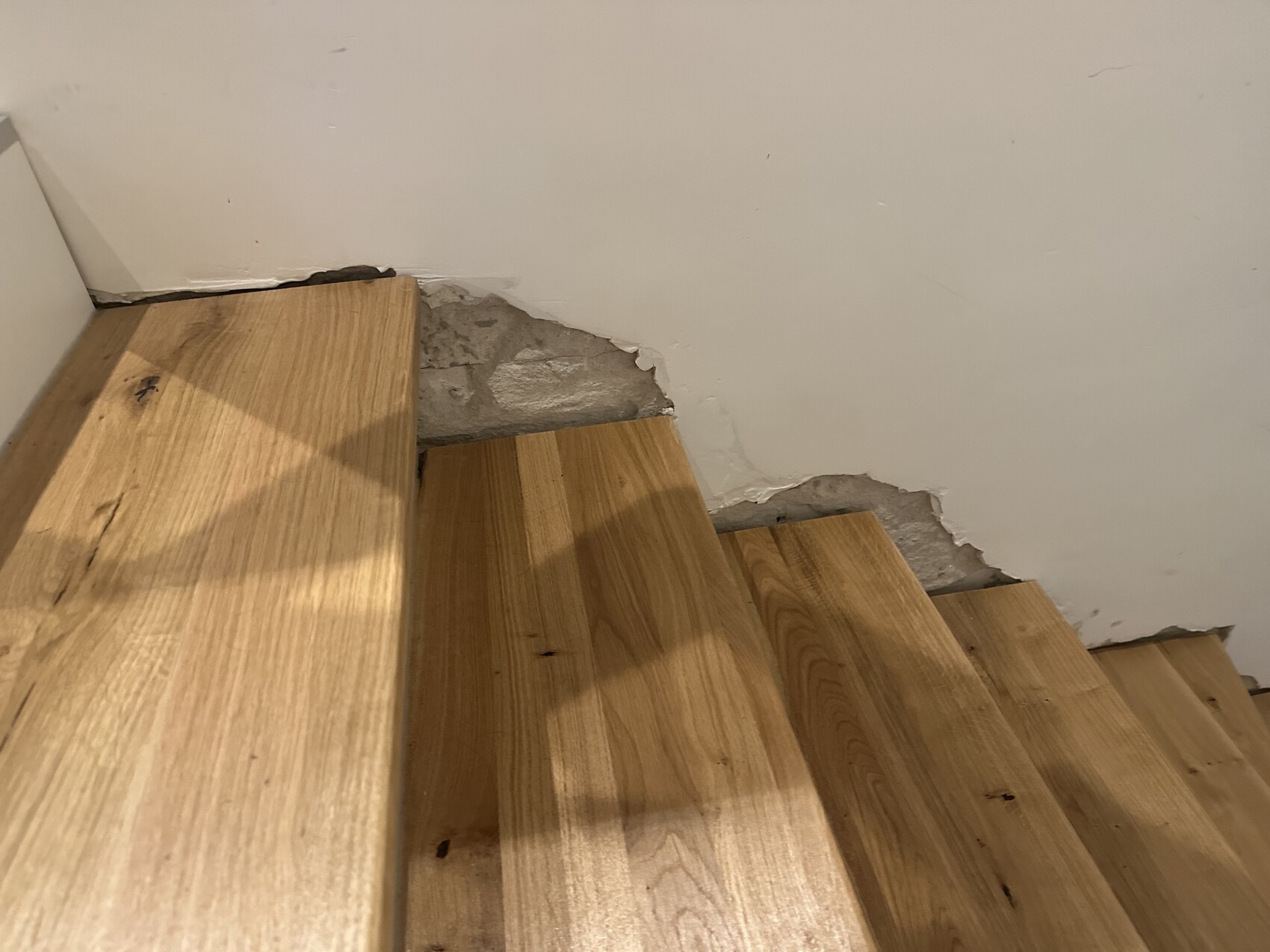 Holztreppe in einem Raum, Wand mit Rissen und bröckelndem Putz hinter den Stufen.