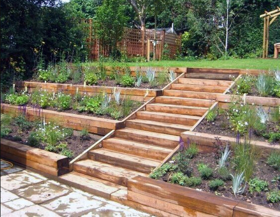 Mehrstöckiges Holzterrassen-Gartenbeet mit Treppenaufgang und Pflanzen.