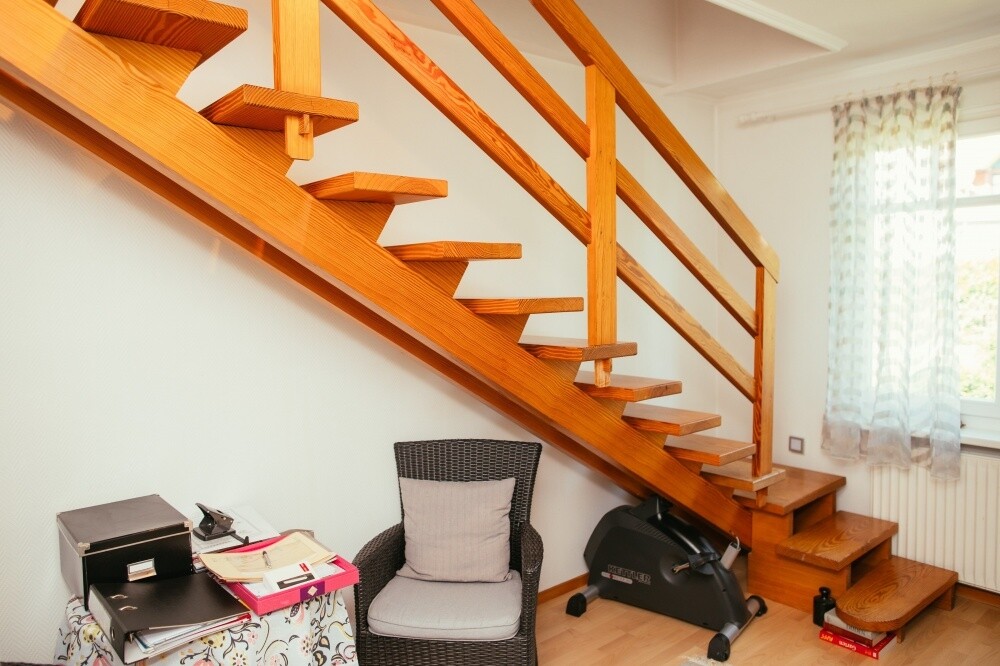Helle Holztreppe mit offenen Stufen im Innenraum neben Sitzbereich und Fenster.