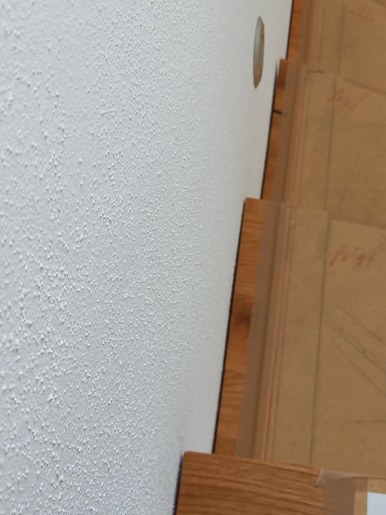 Weiße, grob strukturierte Wand neben einer Holztreppe; Loch in der Wand.