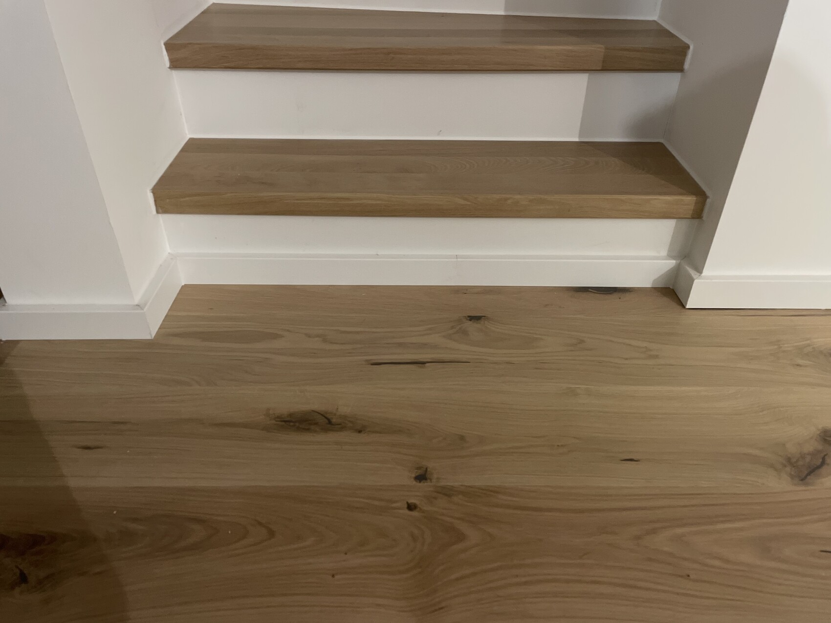 Holzstufen einer Treppe in einem Innenraum, weiße Wände und Holzfußboden.