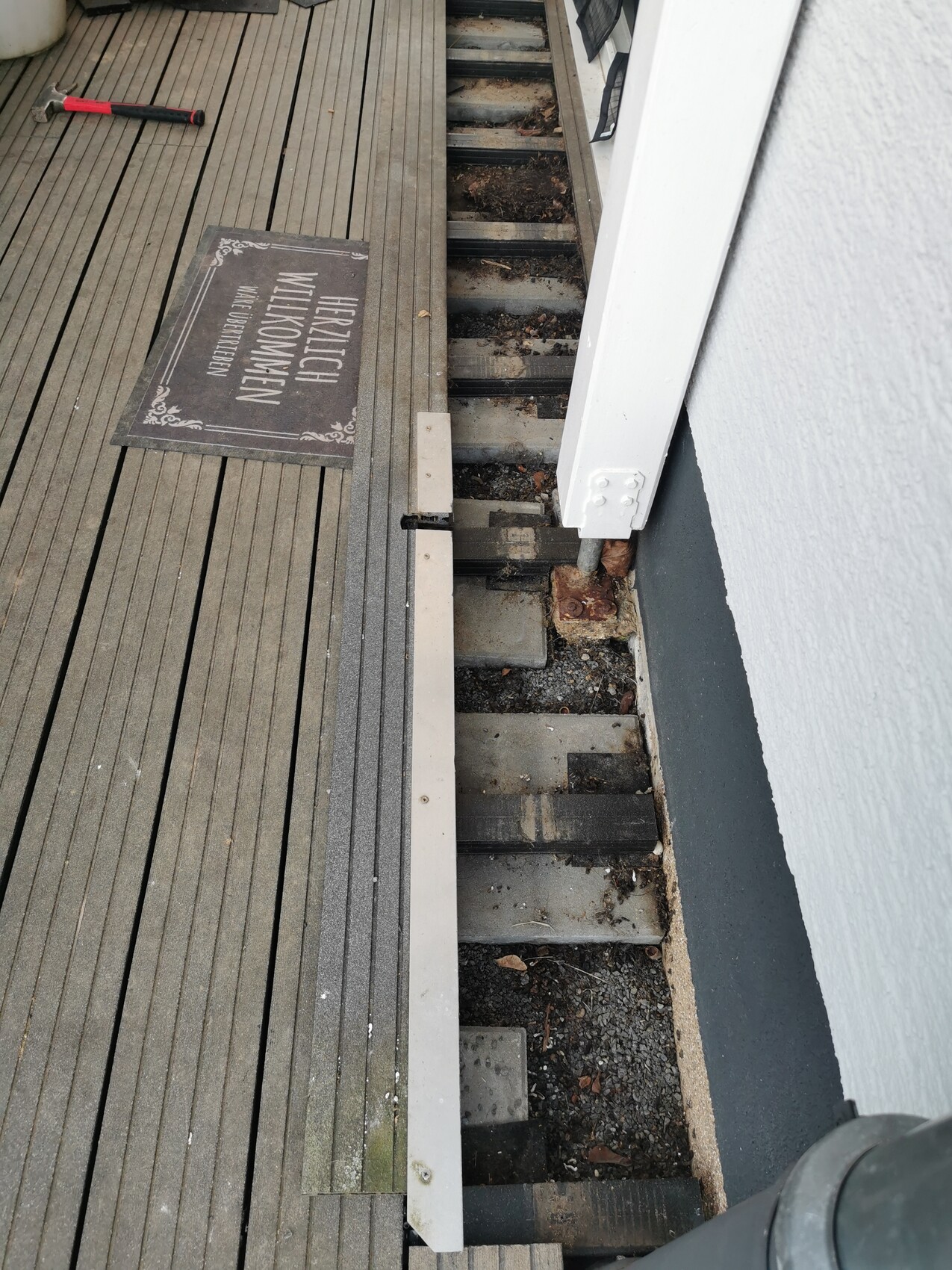 Holzdeck mit Willkommensmatte; offenes Unterdeck mit Stützen, Hammer links.