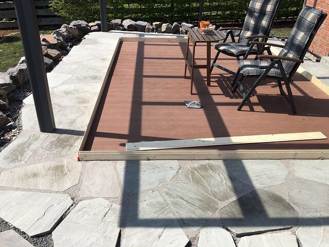Holzterrasse mit zwei gepolsterten Klappstühlen und Beistelltisch auf Steinboden.