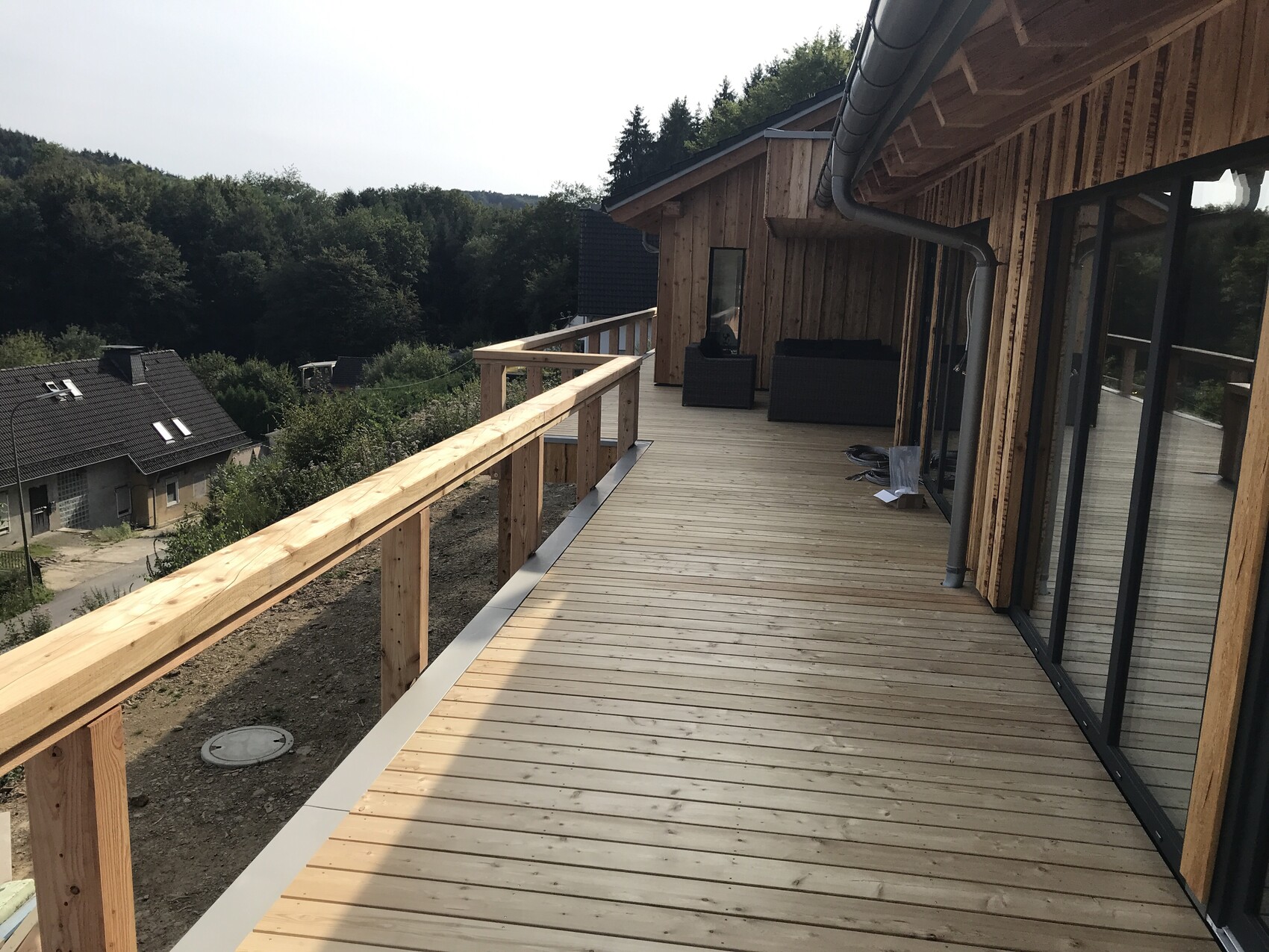 Holzterrasse am Haus mit Geländer, Glastüren, Outdoor-Möbel, Waldblick.