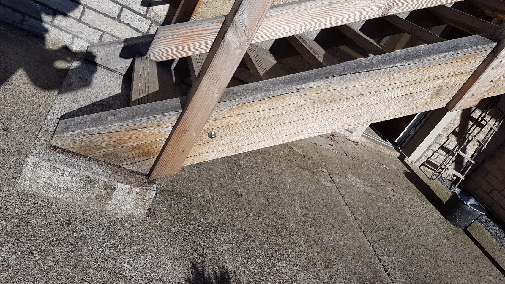 Außenbereich mit rohen Holzbalken einer Treppenkonstruktion auf betonierter Fläche.