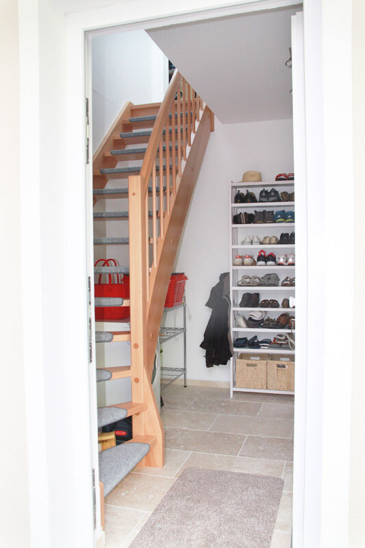Flur mit Holztreppe, Schuhregal voller Schuhe und Mantel im Eingangsbereich.