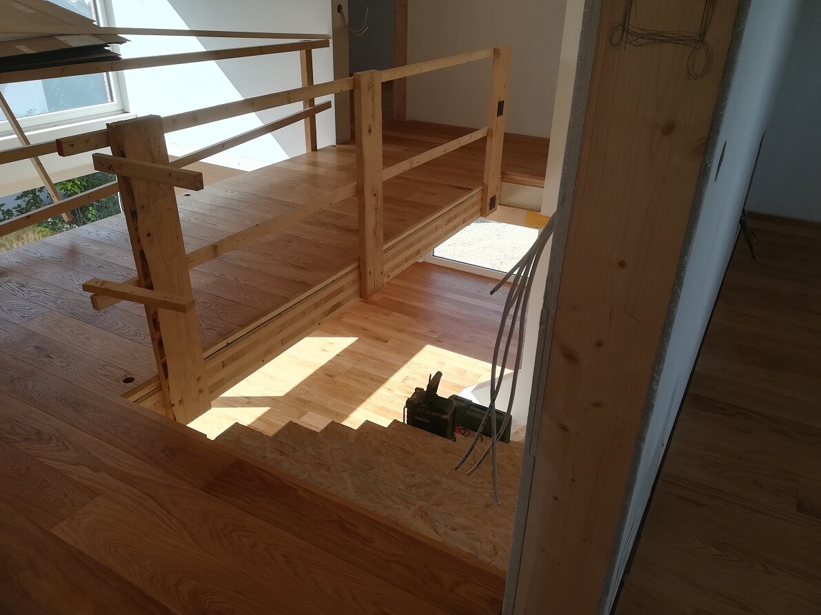 Offene Holzbaustelle: Treppe, Geländer und Holzboden; Kabel liegen auf dem Boden.