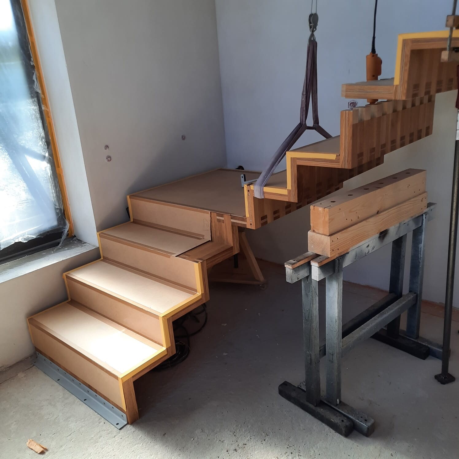 Teilweise montierte Holztreppe in Bauwerkstatt, Kranband hängt über die Stufen