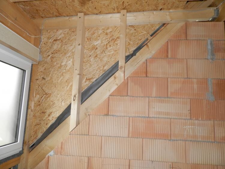 Baustelle: Holzständerwerk, OSB-Verkleidung, diagonale Treppenkonstruktion, Ziegelwand rechts.