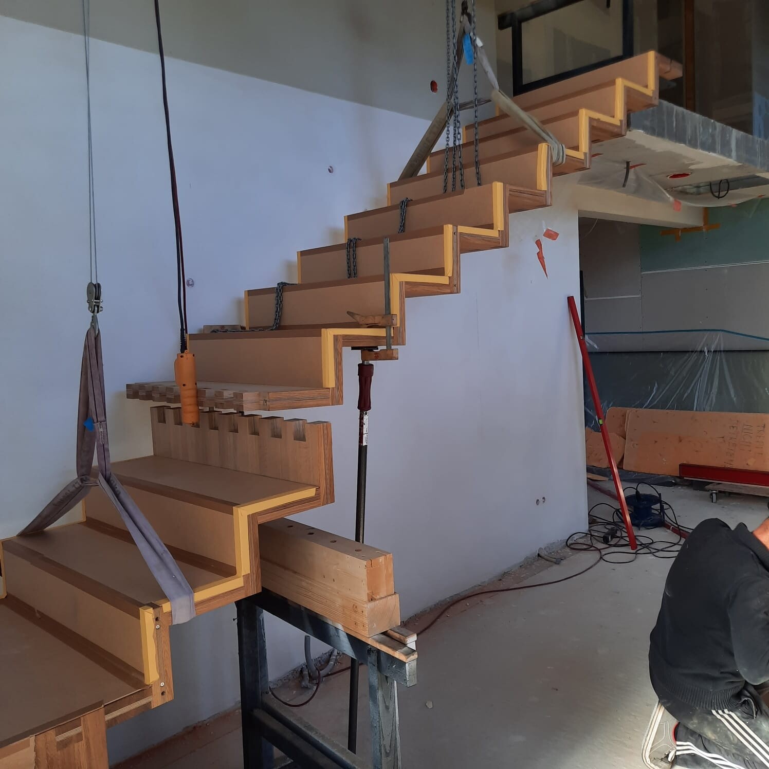 Freitragende Holztreppe im Bau, Zickzack-Form, an Stahlketten aufgehängt.