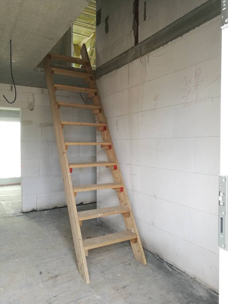 Provisorische Holztreppe in unfertigem Innenraum mit Betonwänden, Bauzustand.