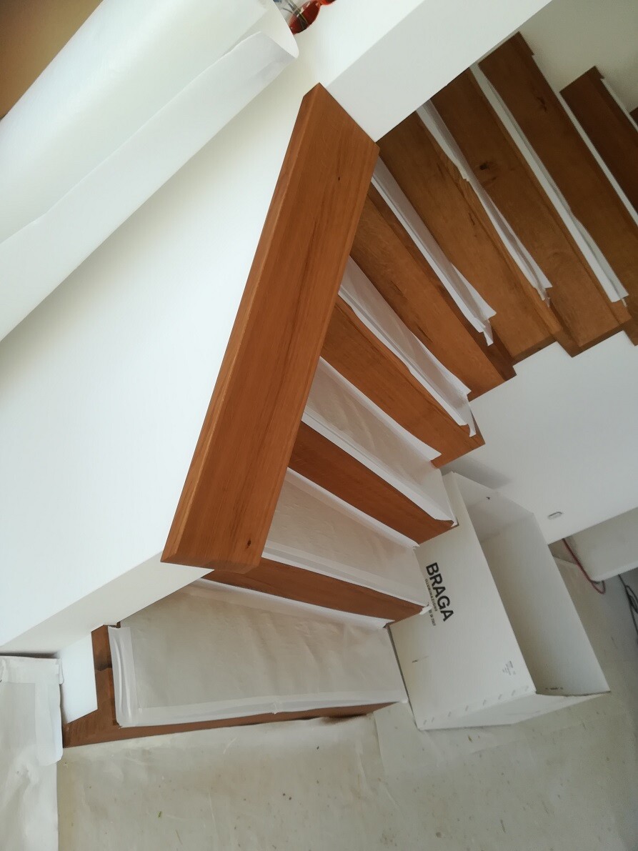 Moderne Innentreppe aus braunen Holzstufen an weißer Wand.