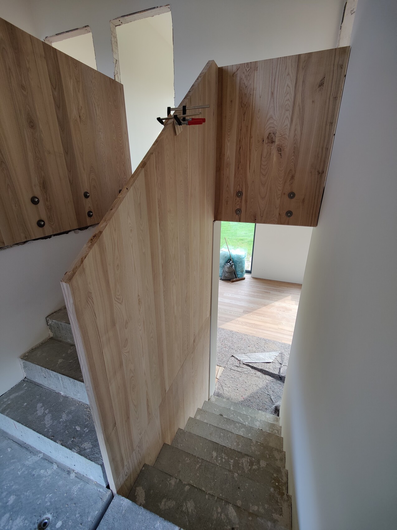 Baustelle: Holzverkleidete Treppenwand, Klemmen an Paneel, offener Durchgang nach Garten.