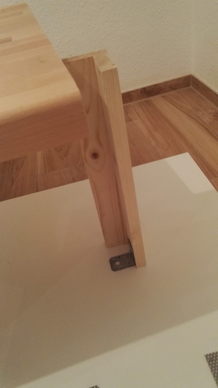 Nahaufnahme einer Holztreppe im Innenbereich mit Pfosten und Metallbeschlag auf Bodenplatte