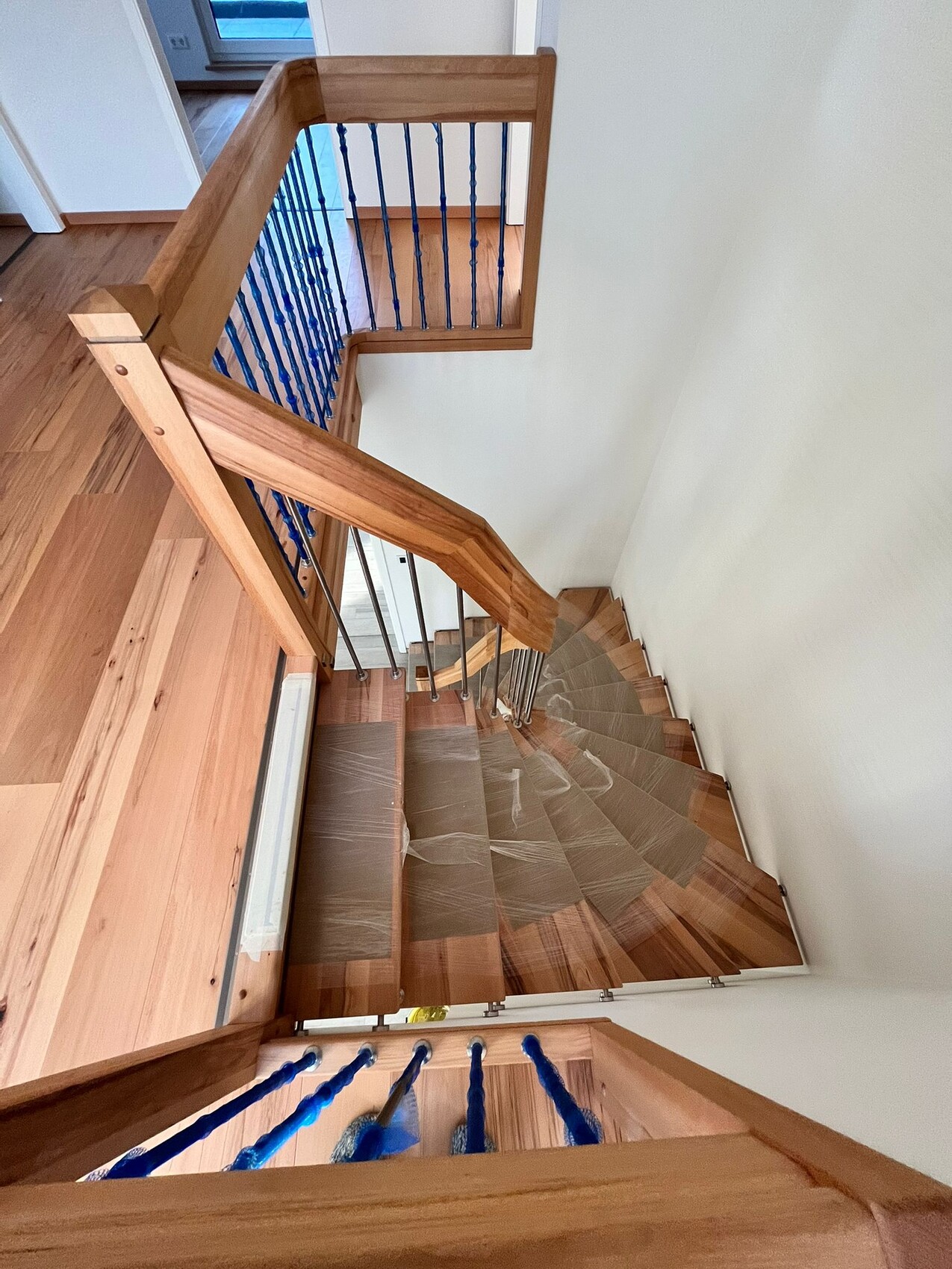 Innenansicht einer mehrstufigen Holztreppe mit blauen Spindeln und Holzgeländer