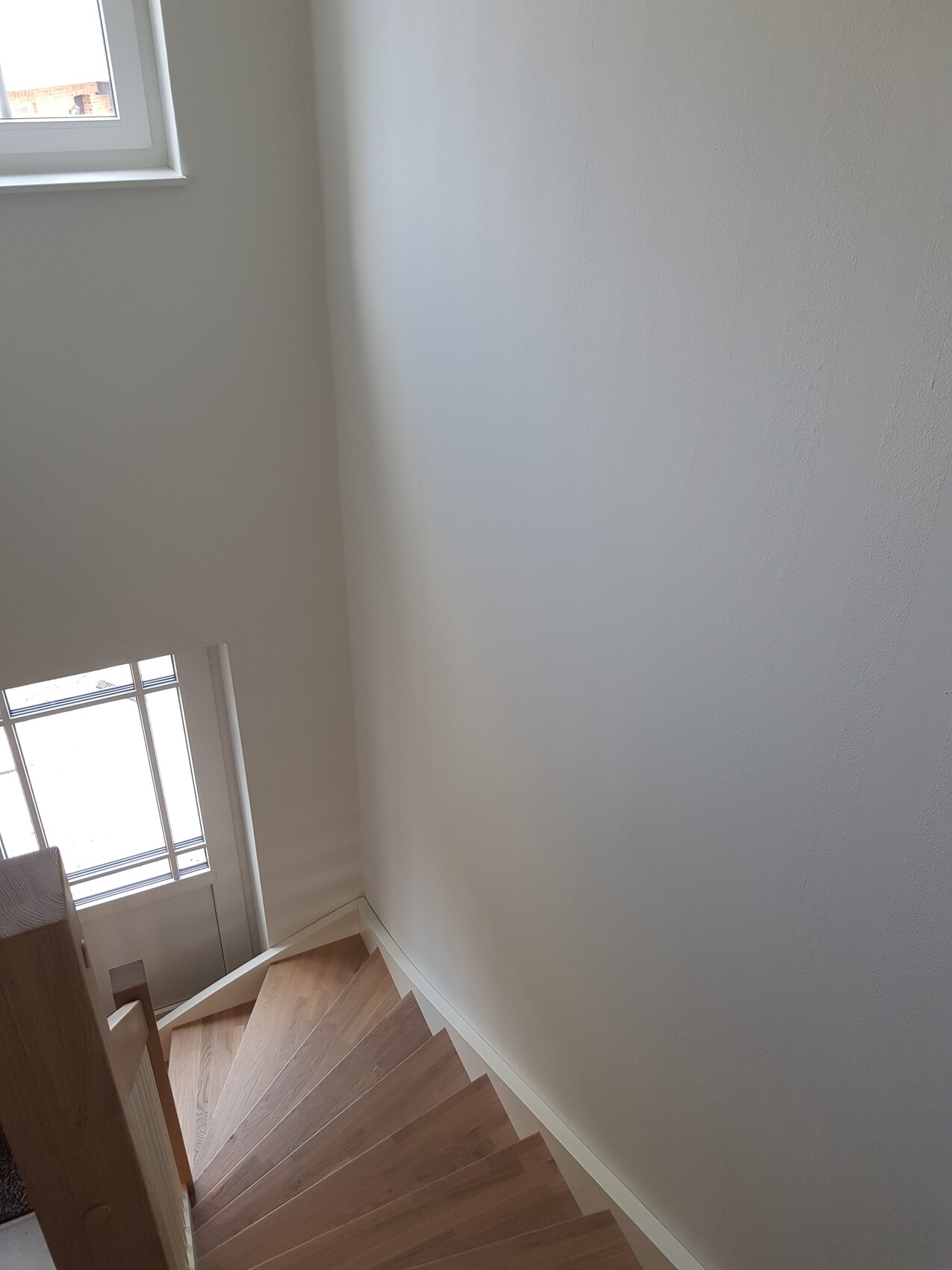 Treppenaufgang mit Holzstufen, weißen Wänden, Fenster links oben.