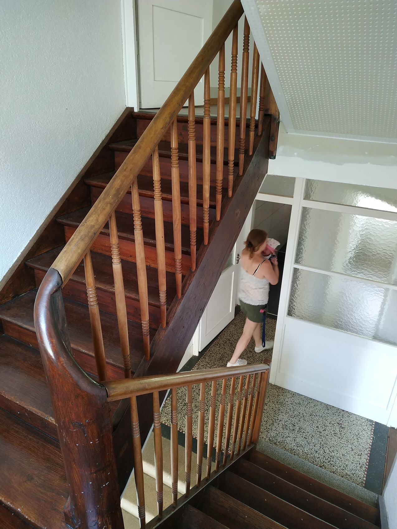 Innenansicht einer dunklen Holztreppe mit Geländer; Frau steigt die Treppe hinab.