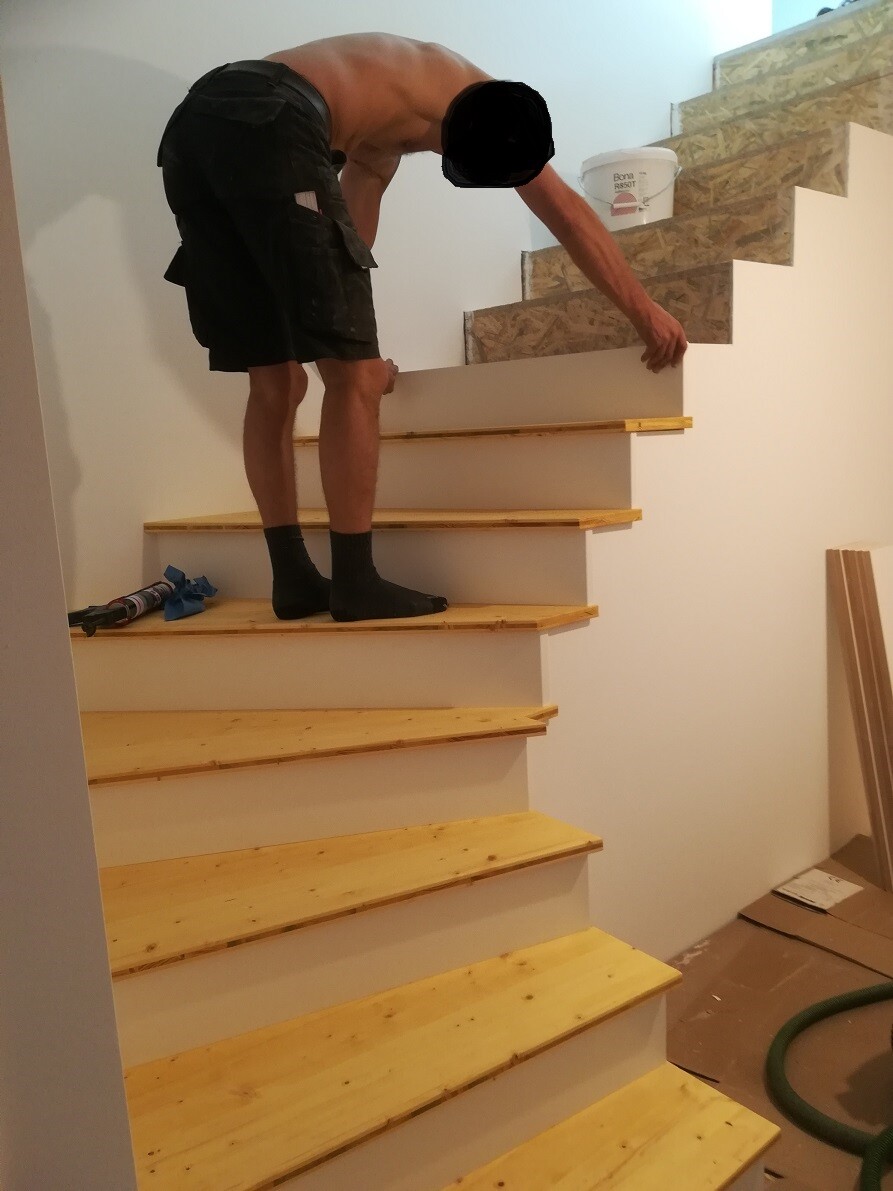 Handwerker montiert Holzstufen an einer Treppe im Bau, daneben Bauwerkzeuge