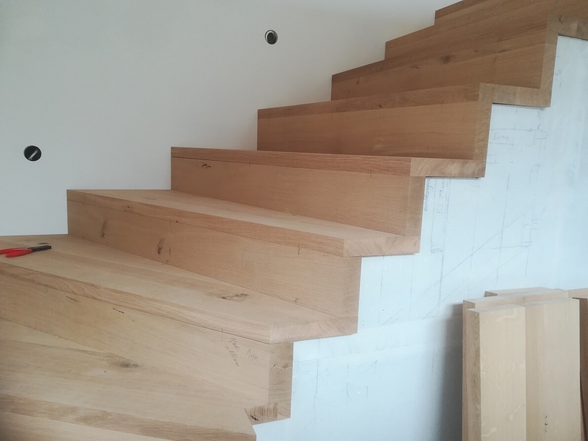 Moderne Holztreppe im Bau, offene Stufen aus Eichenholz, Wand mit Markierungen.