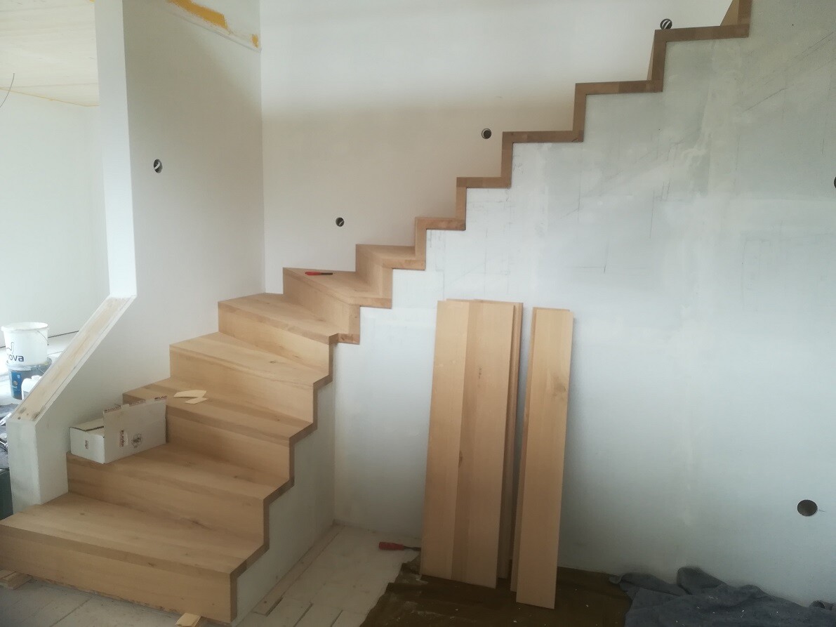 Helle Holztreppe im Bauzimmer, neben Bretterstapeln und Eimer auf der Baustelle.