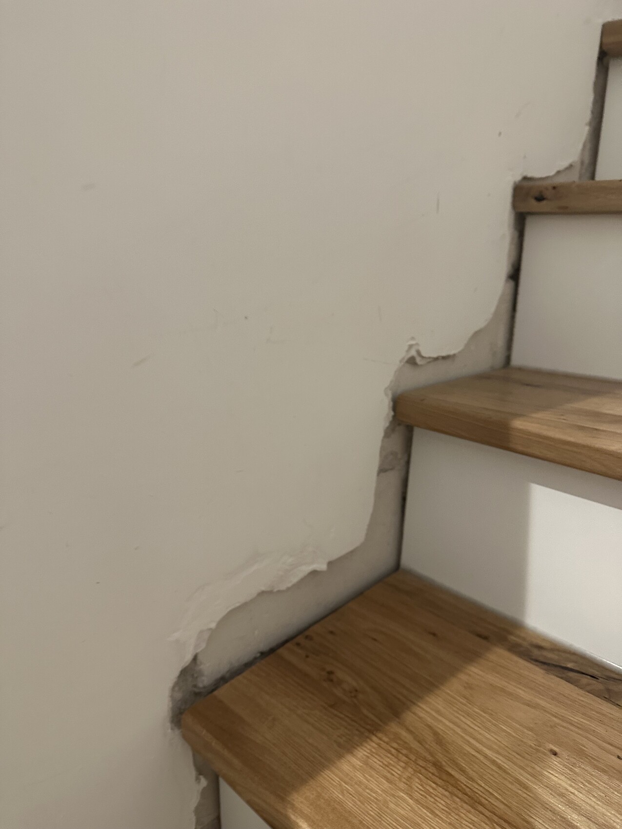 Holzstufen einer Treppe; linke Wand mit abgeblättertem Putz und kleinen Rissen.