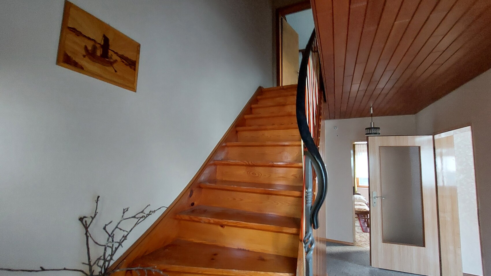 Holztreppe im Flur mit Geländer, offenes Tür zum Schlafzimmer, Wandbild links, Trockenäste am Boden.