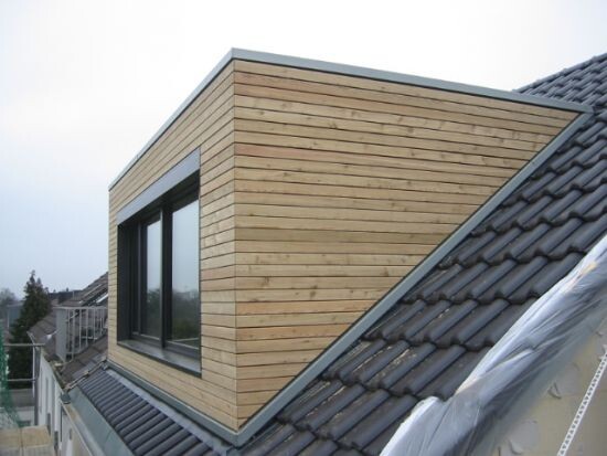 Moderne holzverkleidete Dachgaube mit großem Fenster auf schrägem Ziegeldach.