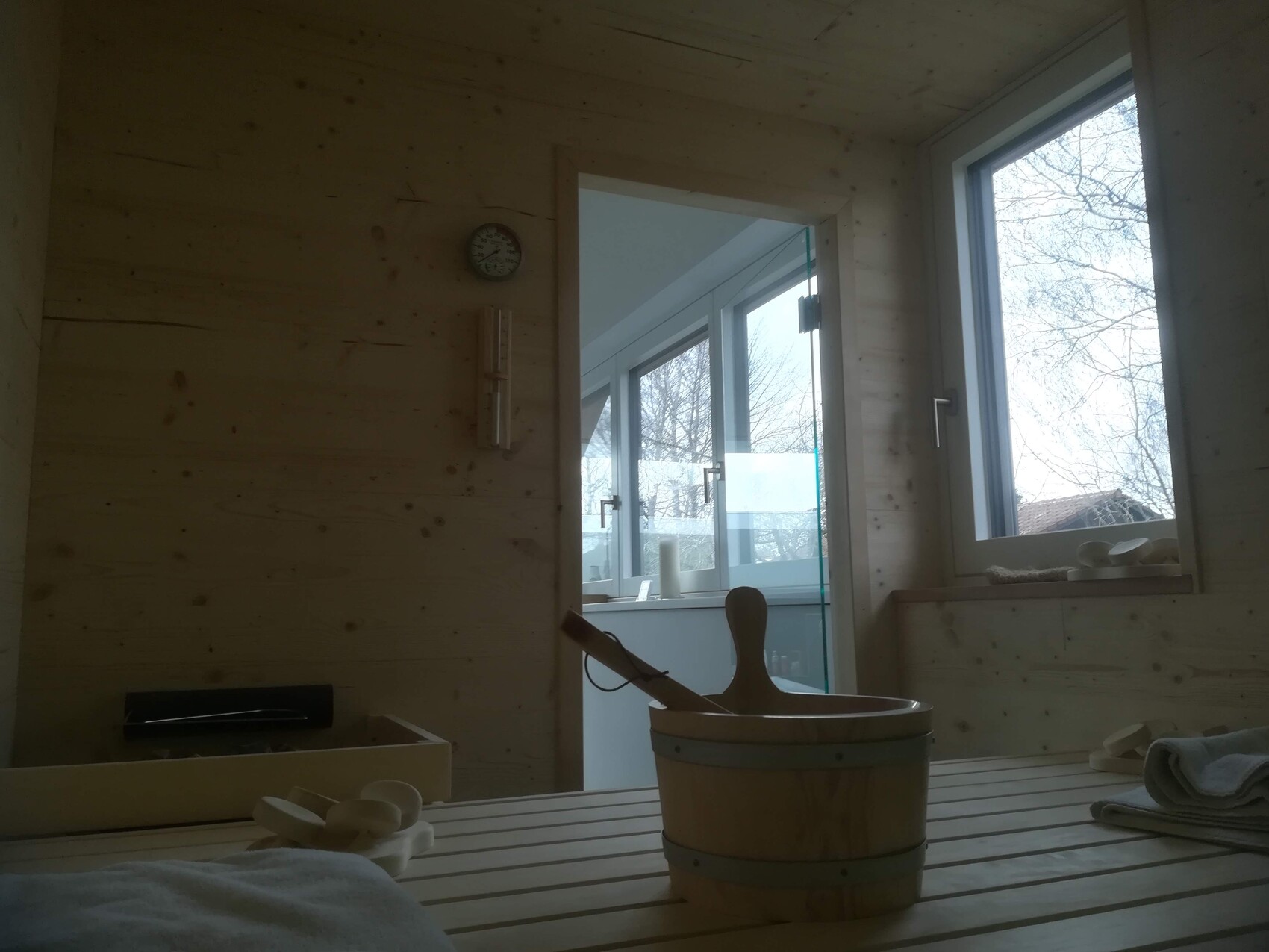 Holzsauna mit Eimer und Löffel auf Bank; Fenster mit Außenblick.