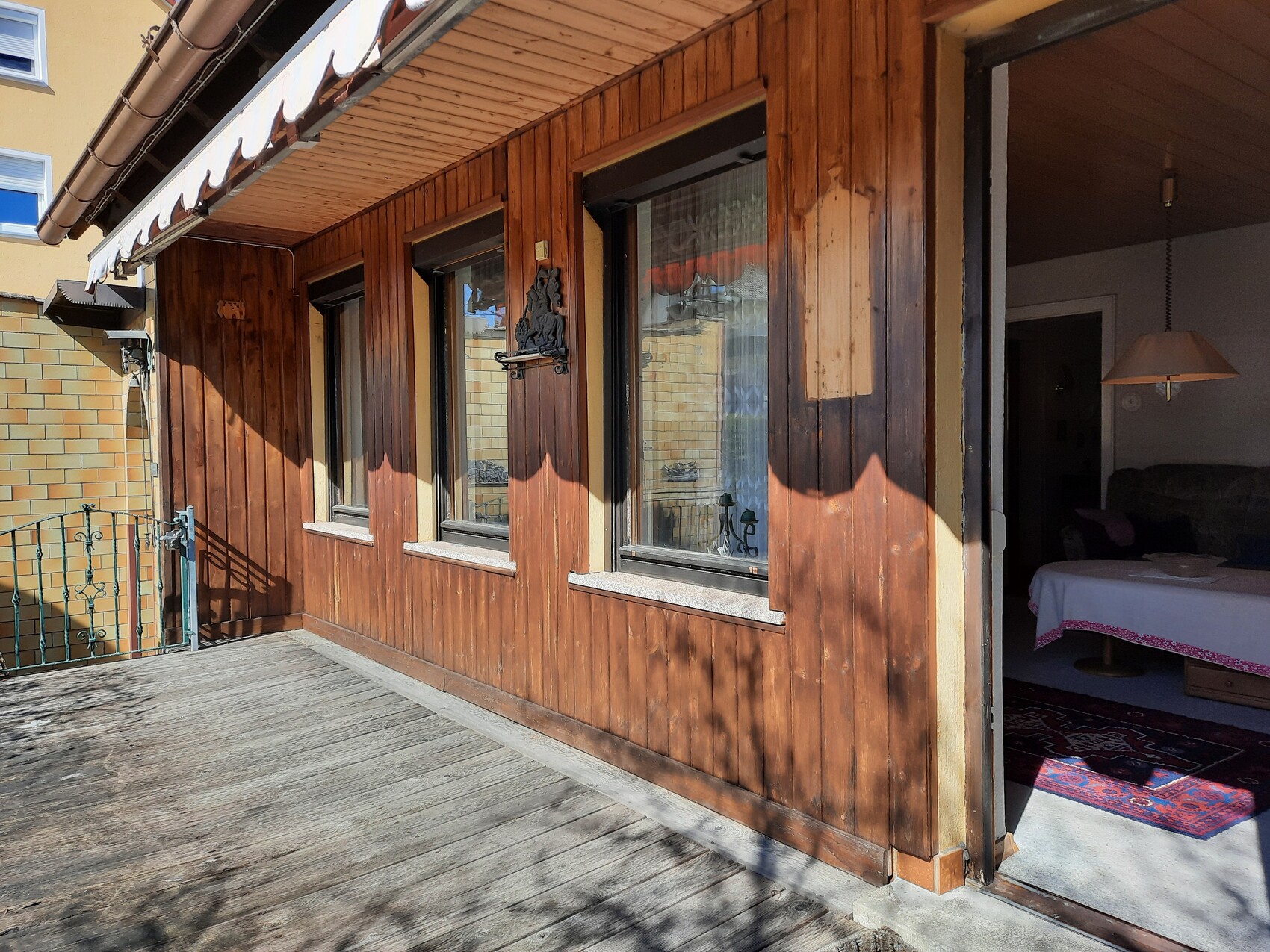 Holzverkleidete Fassade eines Balkons mit drei Fenstern; offenes Türportal zum Wohnzimmer.