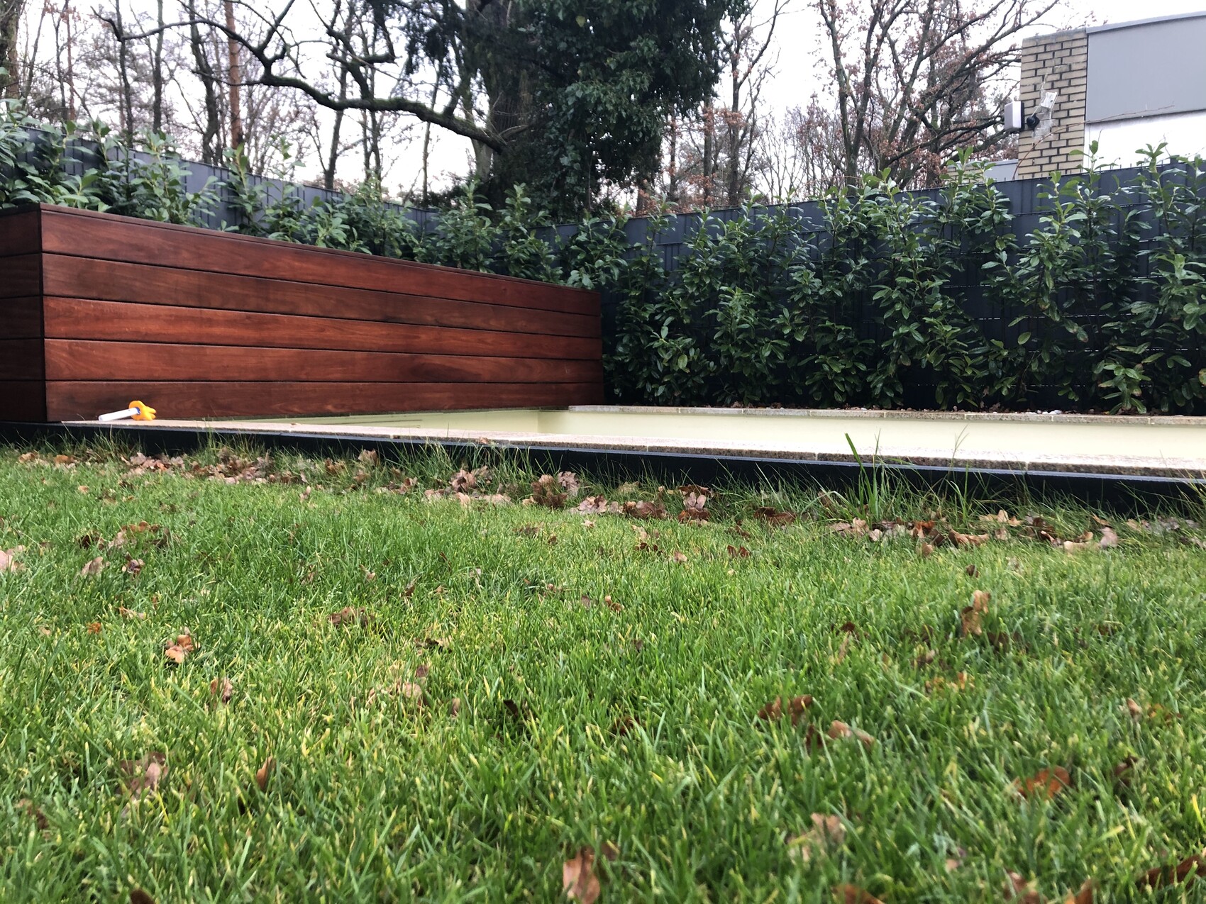 Grüner Garten mit schmalem Wasserbecken, Holz-Pflanzkasten links, Hecke dahinter.