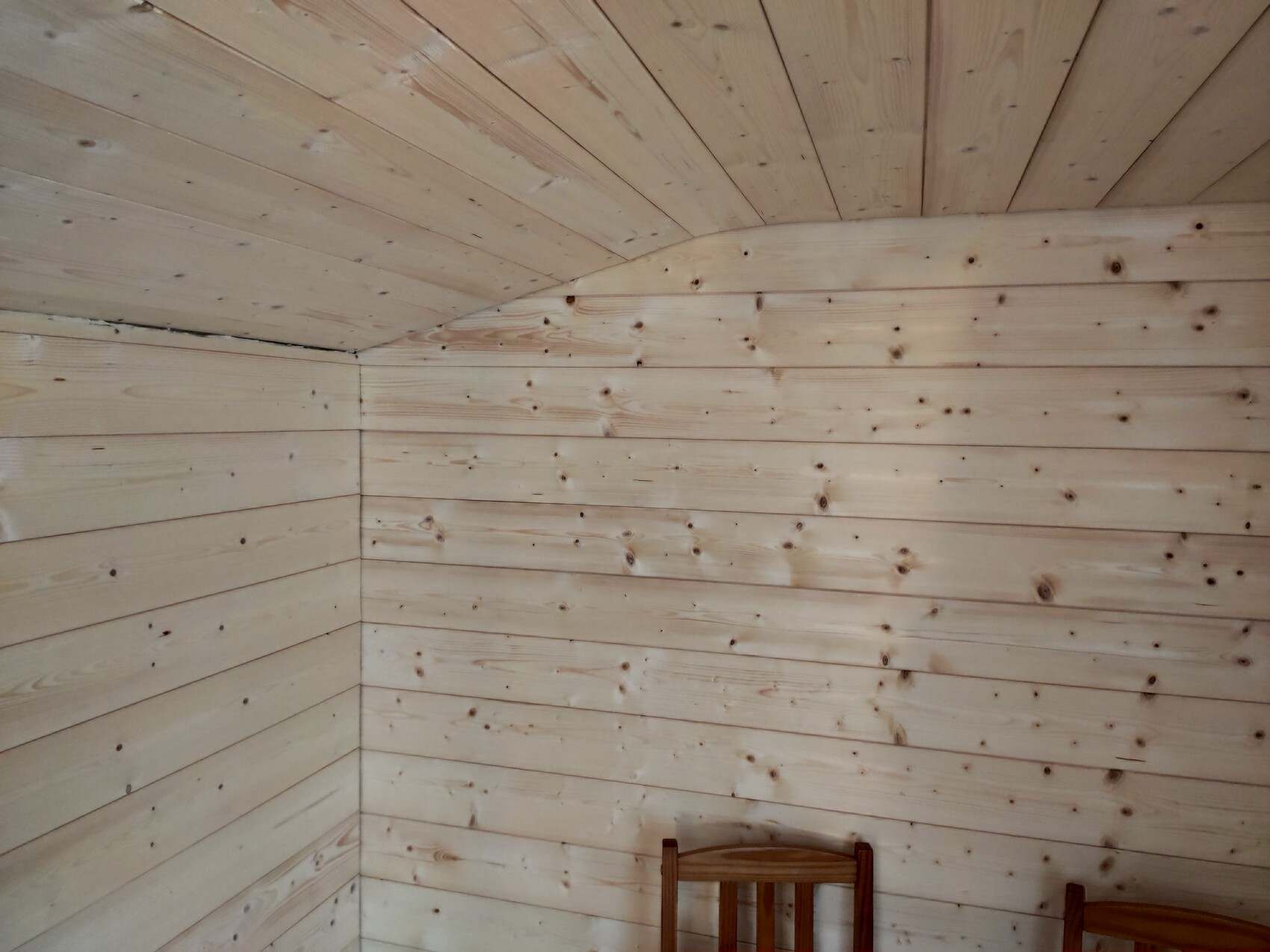 Kleiner Raum mit hellen Holzbrettern an Wänden und Decke, Ecke und zwei Holzstühle sichtbar.