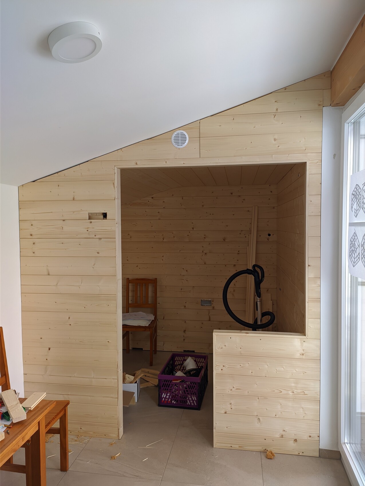 Holzsauna-Bau: offener Raum mit Holzwänden, Eingang, Stuhl und Bauholz.