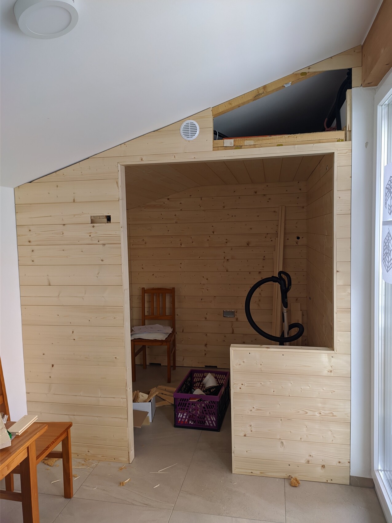 Holzverkleideter Raum unter Dachschräge; Innenraum mit Stuhl, Kiste und schwarzem Schlauch.