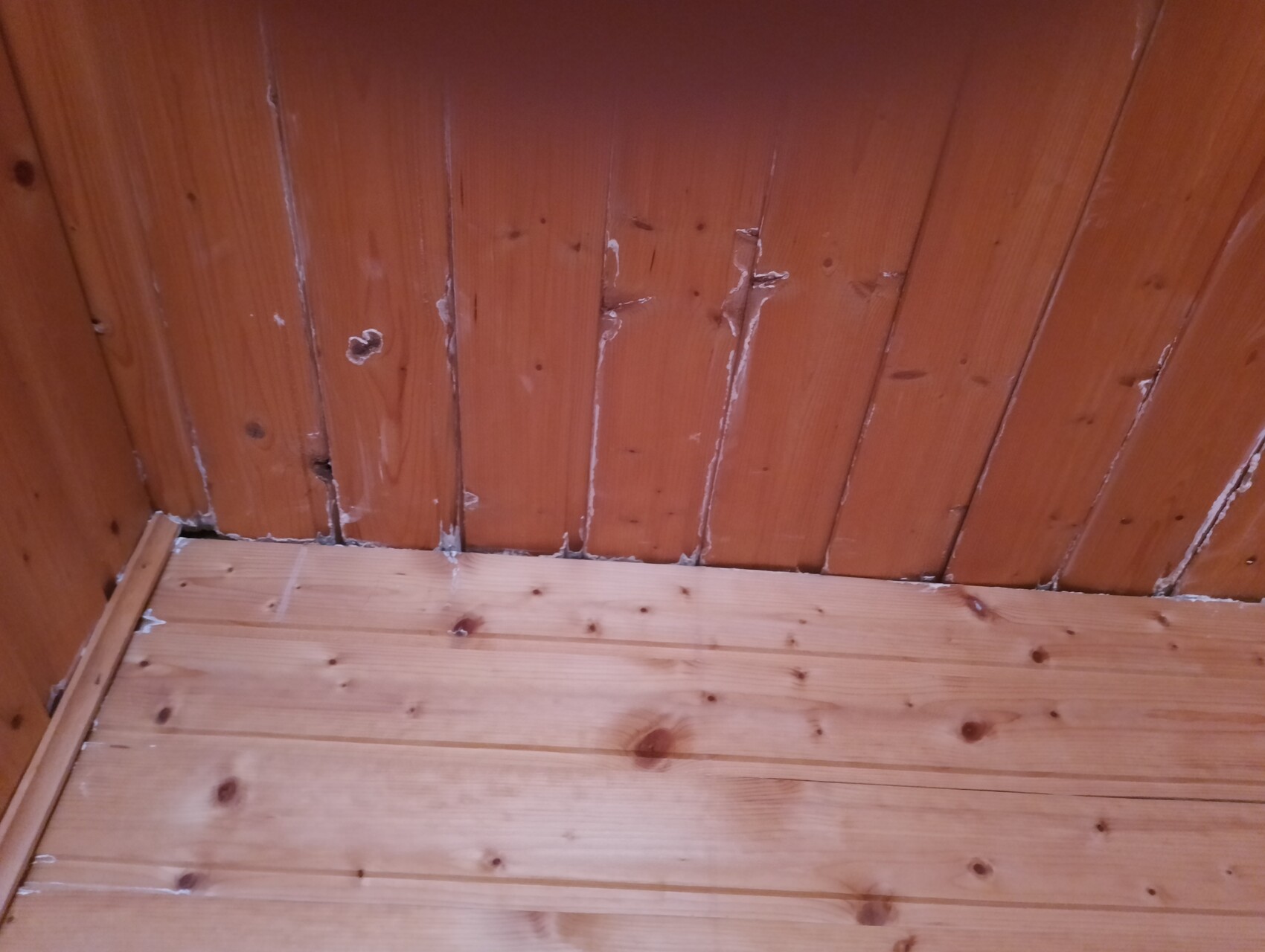 Holzwand und Holzboden in einer Ecke, mit sichtbaren Fugen und Spachtelresten.