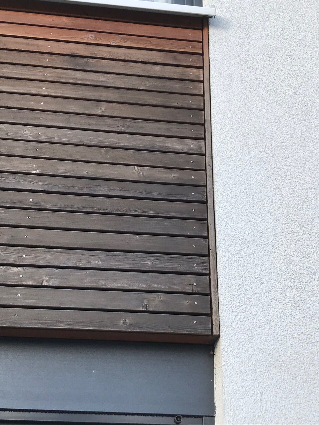 Geschlossene horizontale Holz-Jalousie an hellgrauer Außenwand.