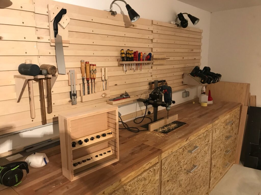 Holzwerkstatt mit Werkbank, Lochwand voller Werkzeuge, Bohrmaschine und Hämmer.