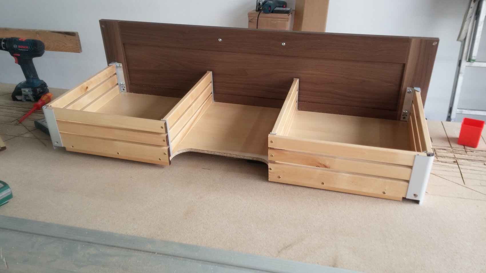 Holzbettgestell mit dunklem Kopfteil und zwei seitlichen Aufbewahrungskisten in einer Werkstatt