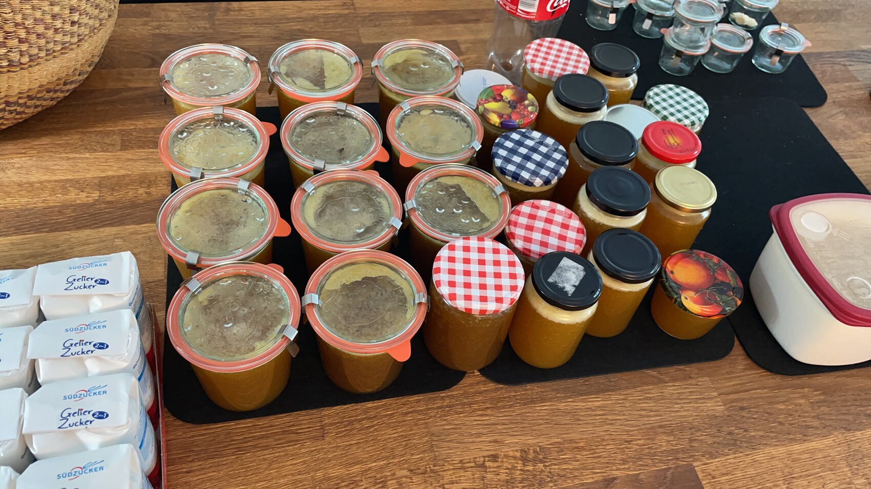 Mehrere Gläser Marmelade mit bunten Deckeln stehen geordnet auf einem Holztisch.