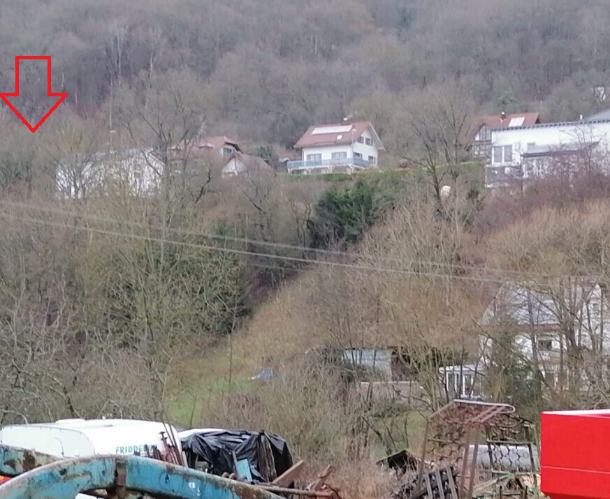 Huegelige Landschaft mit mehreren Gebäuden am Hang und Bauabfällen im Vordergrund